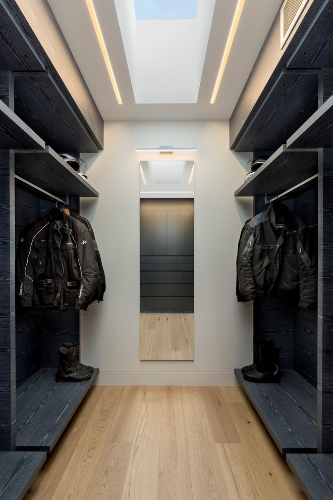 Cette photo montre un grand dressing room tendance pour un homme avec un placard à porte plane, parquet clair, des portes de placard noires et un sol beige.