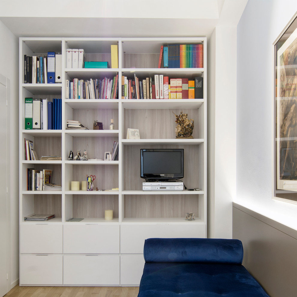 Modelo de despacho contemporáneo pequeño con biblioteca, paredes blancas, suelo de madera clara y escritorio independiente