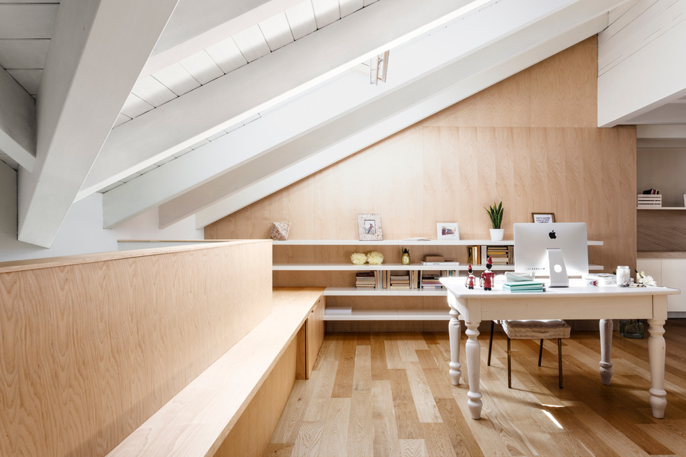 Foto på ett stort funkis hemmabibliotek, med ett fristående skrivbord, beige väggar och mellanmörkt trägolv