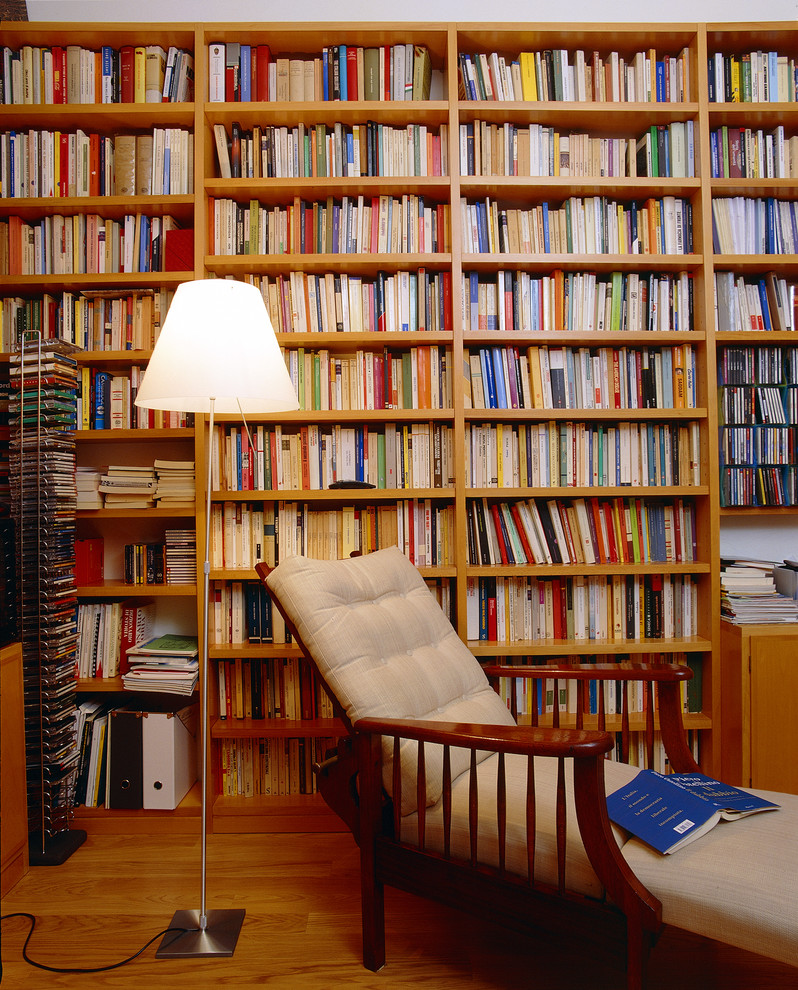Immagine di un grande studio minimalista con libreria, pareti bianche, pavimento in legno massello medio, scrivania autoportante e pavimento marrone