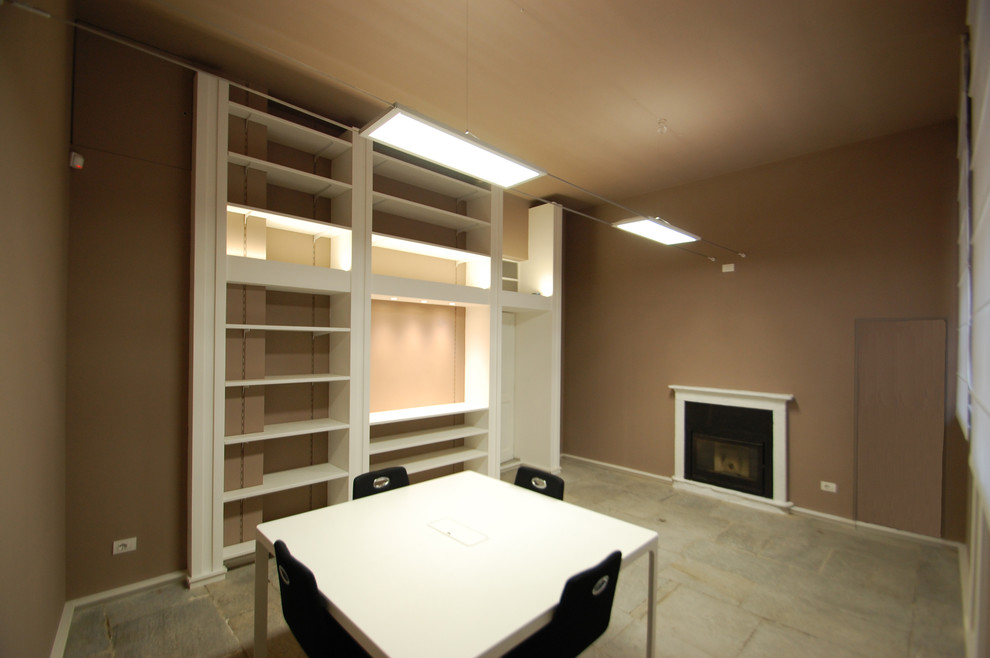 Modern inredning av ett stort arbetsrum, med ett bibliotek, bruna väggar, kalkstensgolv, en standard öppen spis, en spiselkrans i betong, ett fristående skrivbord och grått golv