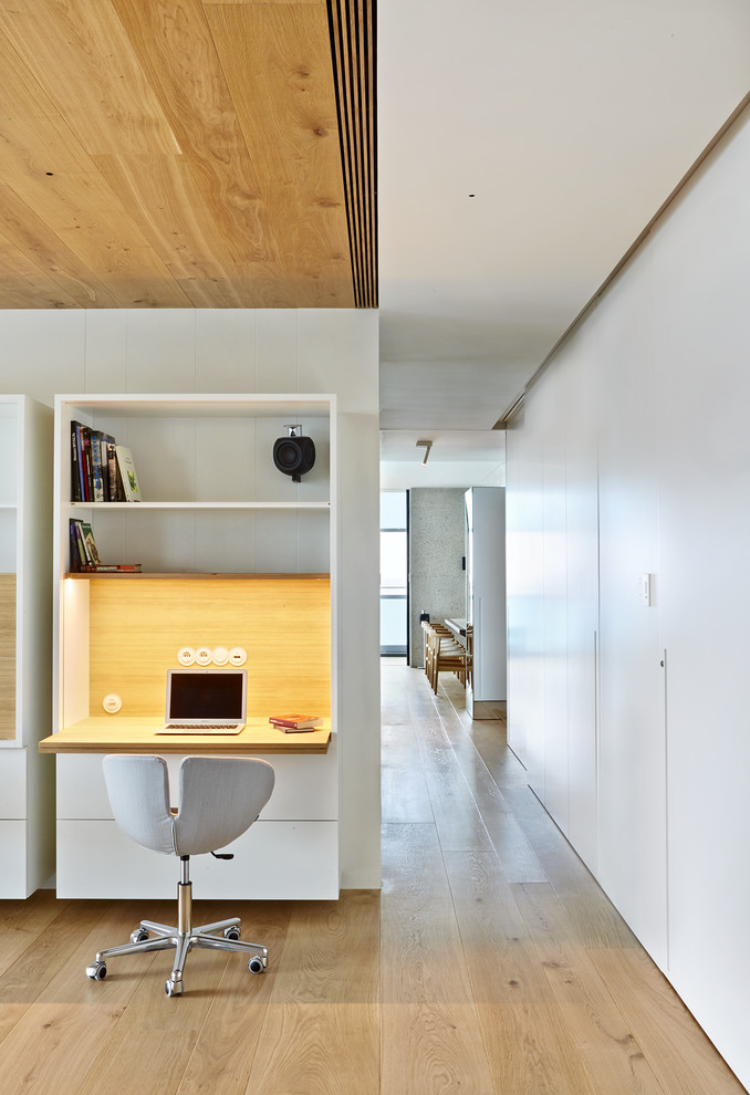 Bild på ett litet funkis hemmabibliotek, med vita väggar, ett inbyggt skrivbord, ljust trägolv och beiget golv