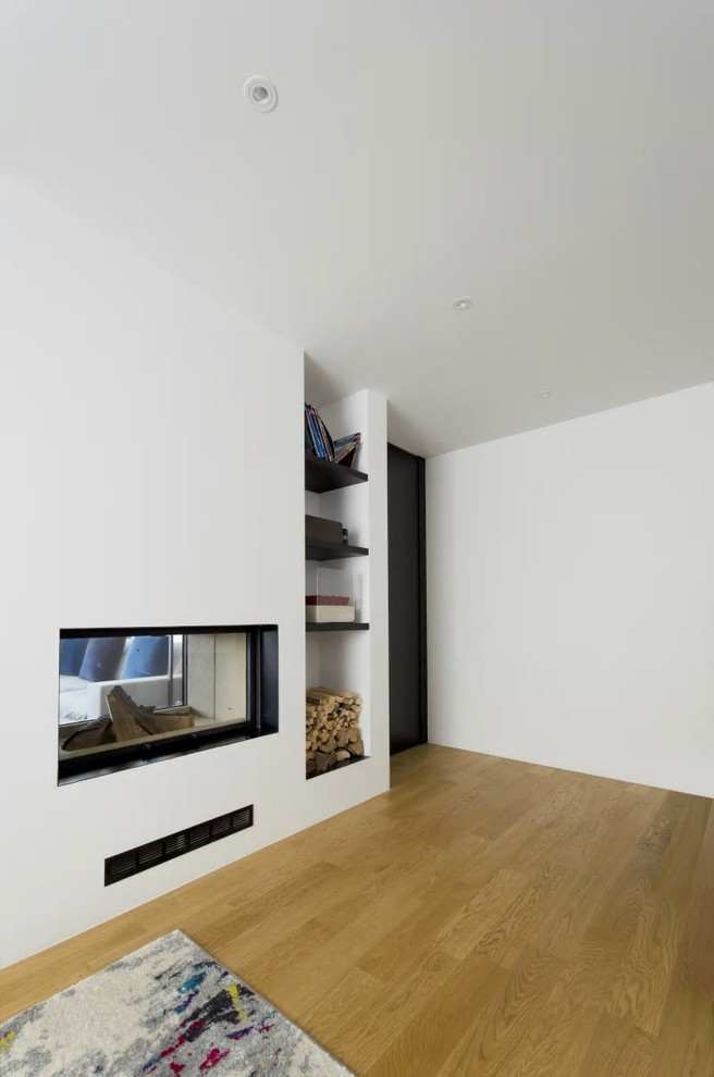 Inredning av ett modernt stort hemmastudio, med vita väggar, ljust trägolv, en dubbelsidig öppen spis, en spiselkrans i gips och brunt golv