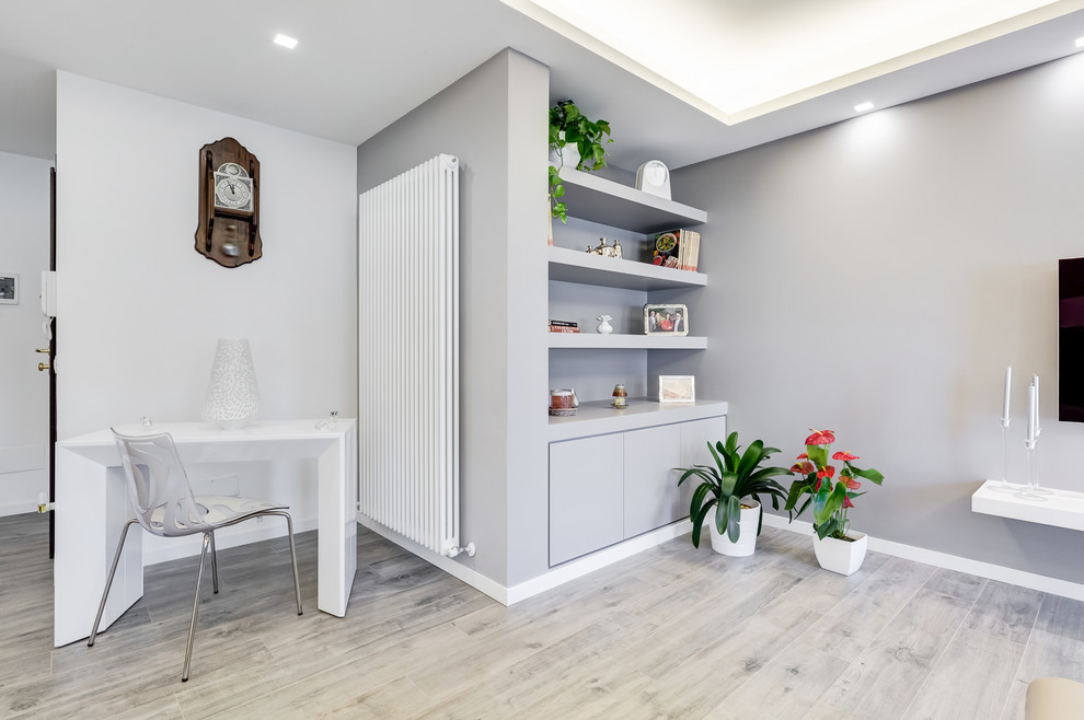 Imagen de despacho moderno pequeño con biblioteca, paredes grises, suelo de madera clara y escritorio independiente