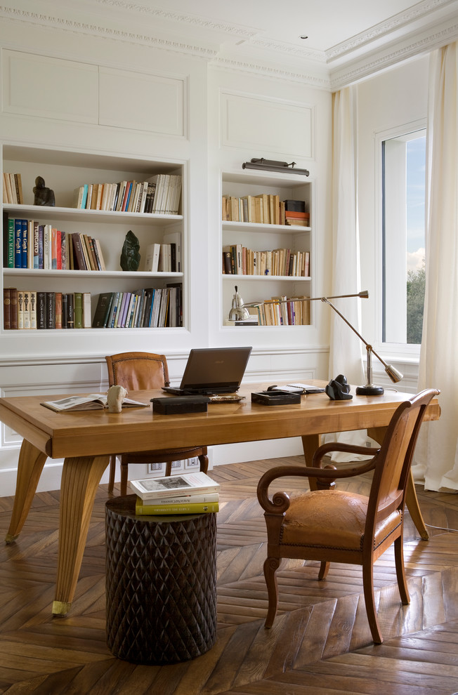 Klassisk inredning av ett hemmabibliotek, med vita väggar, mellanmörkt trägolv och ett fristående skrivbord