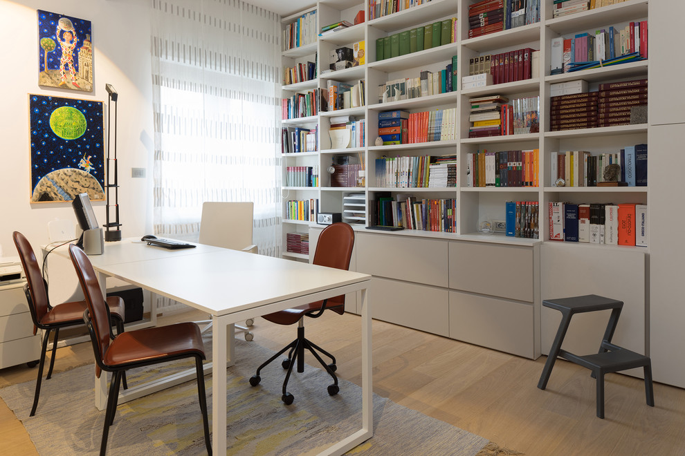 Immagine di un piccolo studio minimal con libreria, pareti bianche, parquet chiaro, scrivania autoportante e pavimento beige