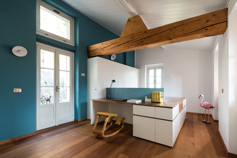 Großes Modernes Arbeitszimmer mit blauer Wandfarbe, Arbeitsplatz, braunem Holzboden und Einbau-Schreibtisch in Mailand