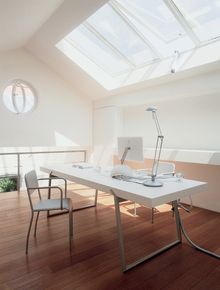 Foto de estudio contemporáneo con paredes blancas, suelo de madera en tonos medios y escritorio independiente