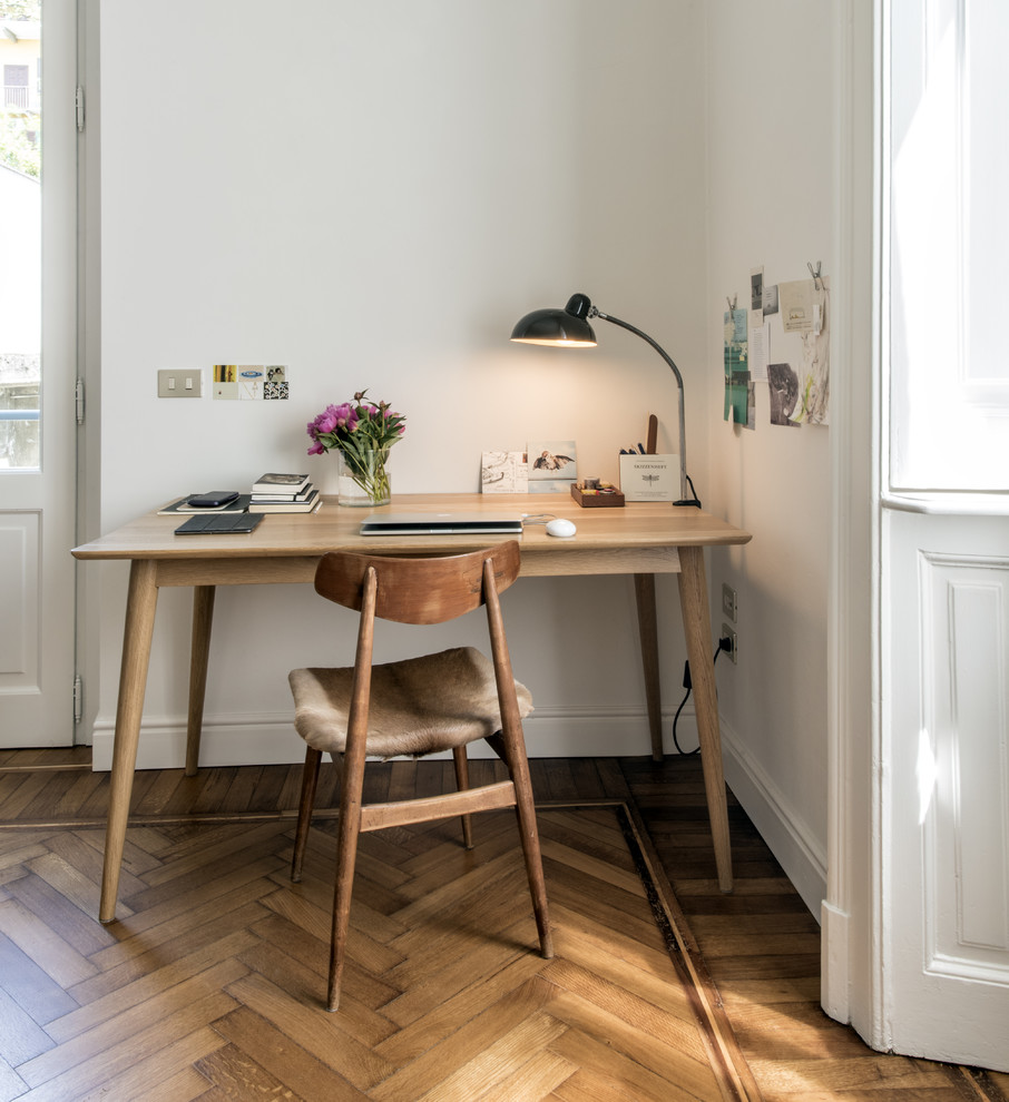 Mittelgroßes Nordisches Arbeitszimmer mit weißer Wandfarbe, braunem Holzboden, freistehendem Schreibtisch und braunem Boden in Mailand