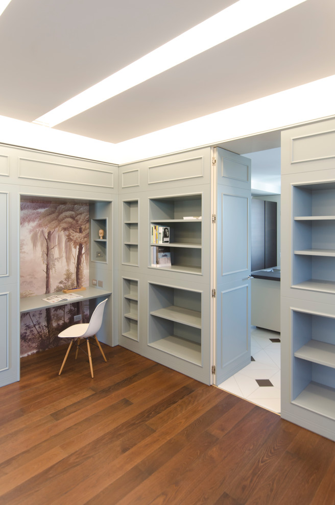 Ejemplo de despacho tradicional extra grande con biblioteca, paredes grises, suelo de madera en tonos medios, escritorio empotrado y suelo marrón
