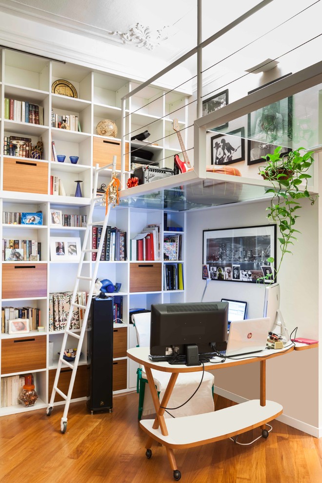 Foto på ett funkis arbetsrum, med ett bibliotek, vita väggar och mellanmörkt trägolv