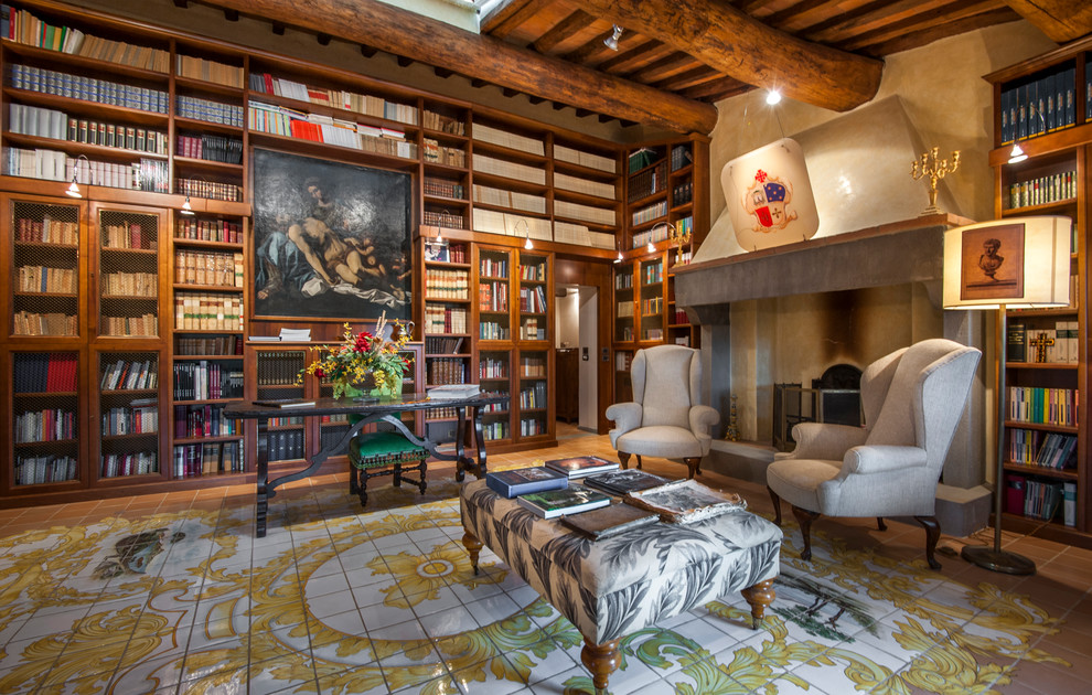 フィレンツェにあるトラディショナルスタイルのおしゃれなホームオフィス・書斎 (ライブラリー、ベージュの壁、標準型暖炉、コンクリートの暖炉まわり、自立型机、マルチカラーの床) の写真