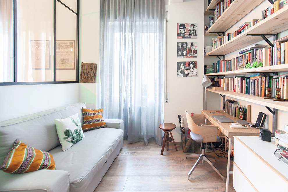 Minimalistisk inredning av ett arbetsrum, med ett bibliotek, vita väggar, ljust trägolv och ett fristående skrivbord
