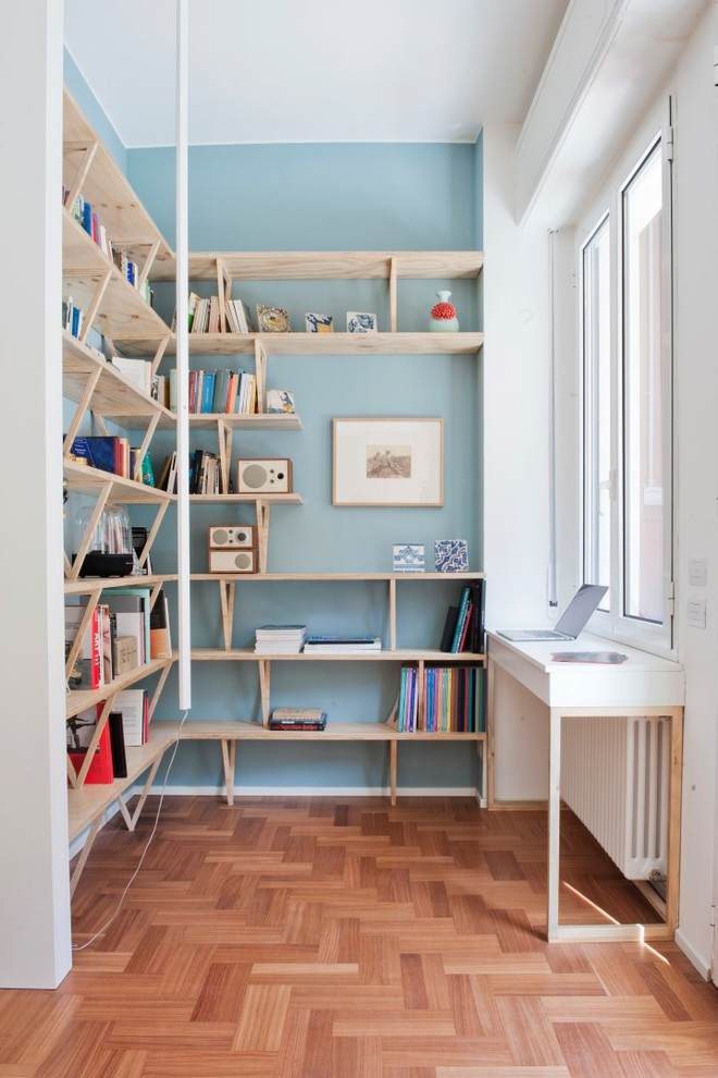 Ejemplo de despacho nórdico de tamaño medio con paredes azules, suelo de madera en tonos medios, biblioteca, escritorio empotrado y suelo marrón