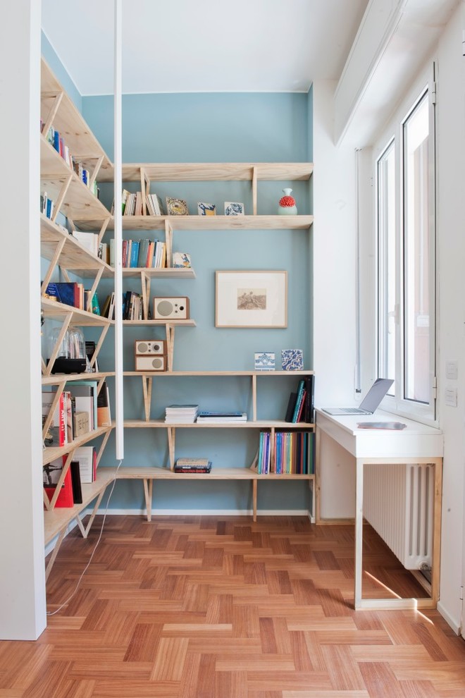 Home office library - mid-sized scandinavian built-in desk medium tone wood floor and brown floor home office library idea in Milan with blue walls