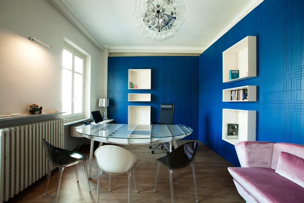 Bild på ett funkis hemmabibliotek, med blå väggar, mörkt trägolv, ett fristående skrivbord och brunt golv