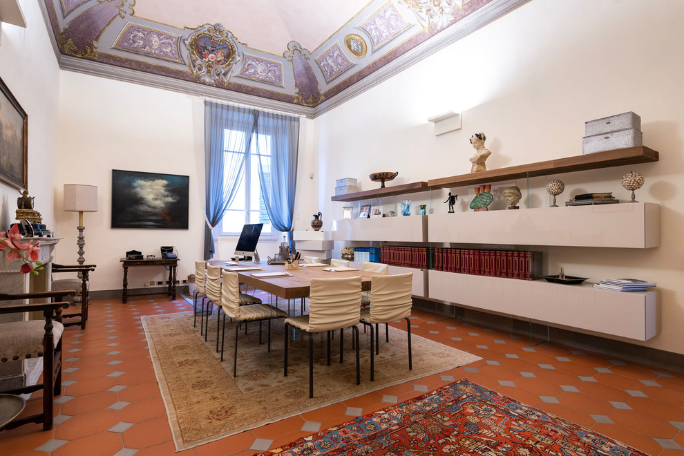 Großes Modernes Arbeitszimmer mit Arbeitsplatz, weißer Wandfarbe, Terrakottaboden, Kamin, Kaminumrandung aus Beton, freistehendem Schreibtisch und braunem Boden in Florenz