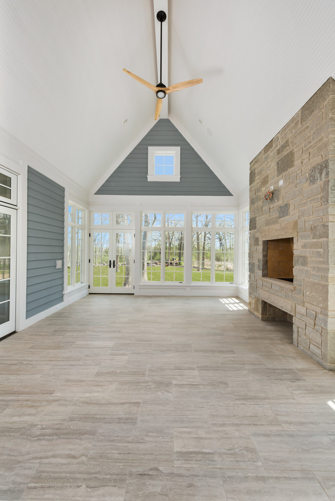 Cette photo montre une grande véranda chic avec un sol en carrelage de céramique, une cheminée standard, un manteau de cheminée en pierre, un plafond standard et un sol gris.