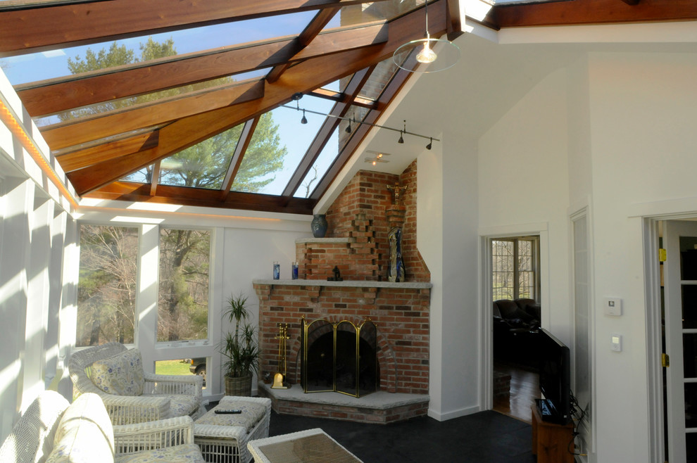 Idee per una veranda contemporanea di medie dimensioni con pavimento in ardesia, camino ad angolo, cornice del camino in mattoni e soffitto in vetro