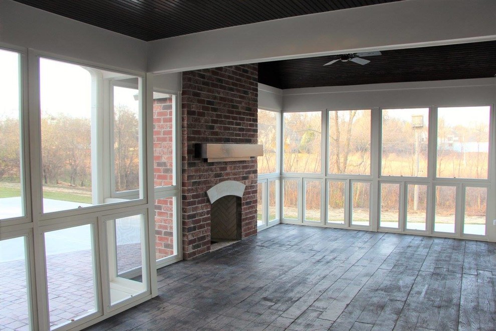 Exemple d'une grande véranda chic avec une cheminée standard, un manteau de cheminée en brique, un plafond standard, sol en béton ciré et un sol marron.