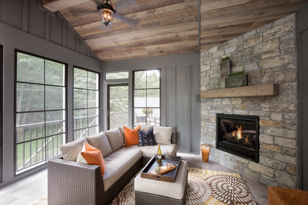 Idée de décoration pour une véranda chalet avec sol en béton ciré, une cheminée standard, un manteau de cheminée en pierre, un plafond standard et un sol gris.