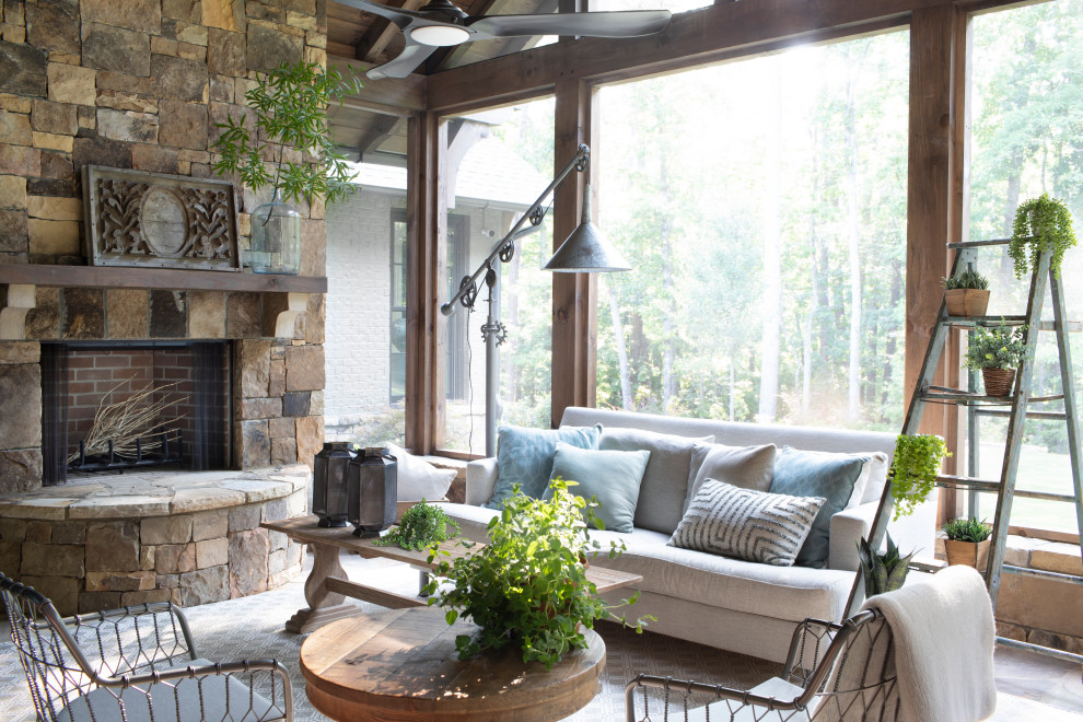 Idée de décoration pour une grande véranda champêtre avec une cheminée standard, un manteau de cheminée en pierre et un plafond standard.