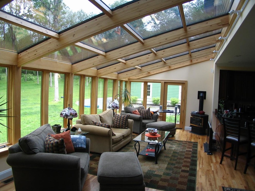 Diseño de galería actual de tamaño medio con suelo de madera clara, estufa de leña, marco de chimenea de metal y techo de vidrio