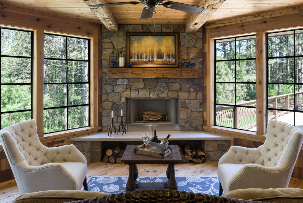 Cette image montre une véranda chalet avec une cheminée d'angle, un manteau de cheminée en pierre, un plafond standard, un sol beige et parquet clair.