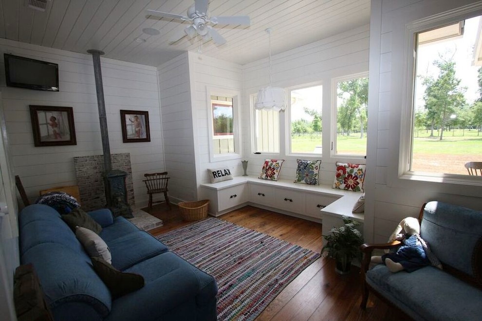 Immagine di una piccola veranda country con pavimento in legno massello medio, stufa a legna, cornice del camino in mattoni, soffitto classico e pavimento marrone