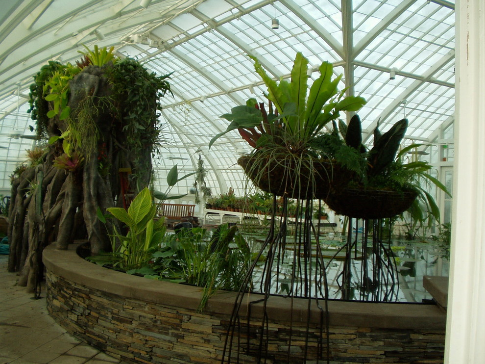 Diseño de galería tropical extra grande con suelo de cemento y techo de vidrio
