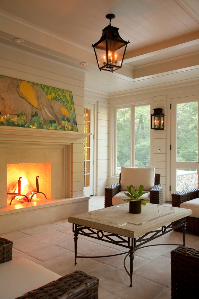 Cette photo montre une véranda chic avec une cheminée standard, un manteau de cheminée en pierre, un plafond standard et un sol beige.
