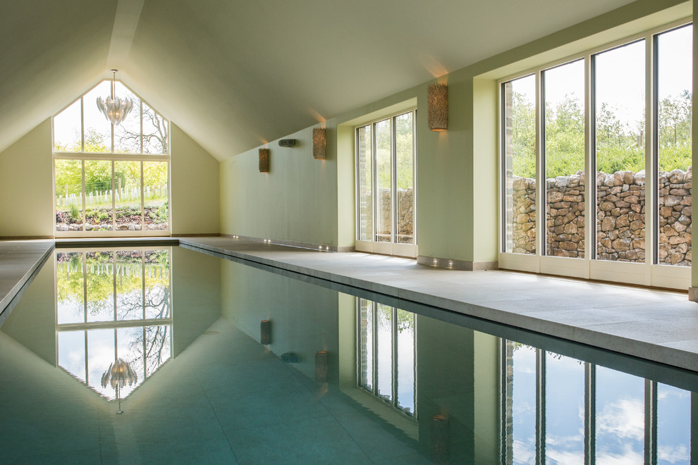 This is an example of a contemporary indoor rectangular lengths swimming pool in Other with a pool house and concrete paving.