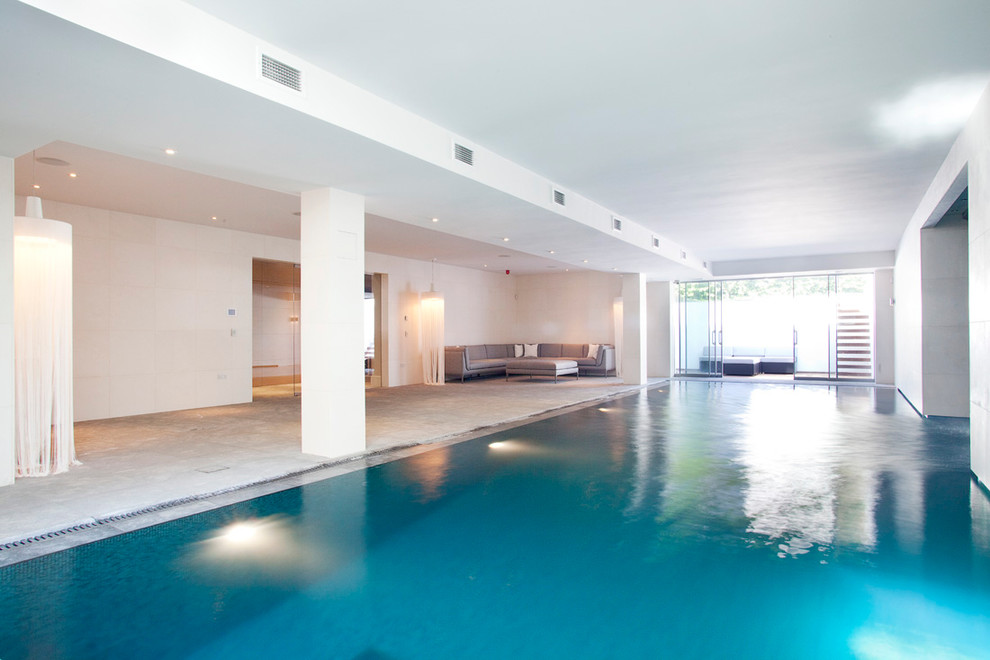 Contemporary indoor rectangular swimming pool in London with natural stone paving.