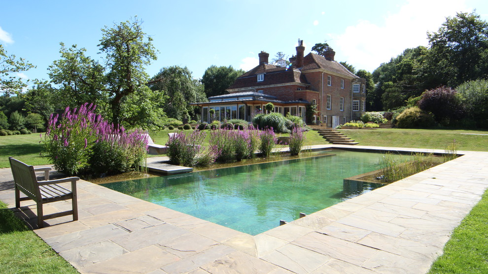 Diseño de piscina con fuente natural rústica grande rectangular en patio trasero con adoquines de piedra natural