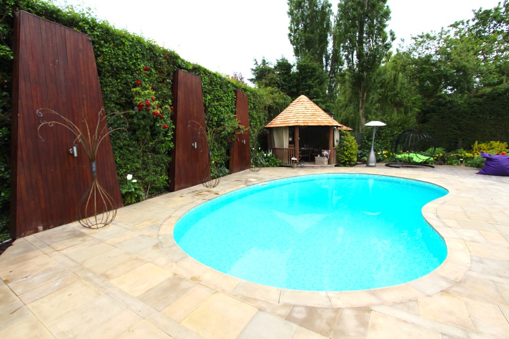 This is an example of a large contemporary back kidney-shaped infinity swimming pool in Essex with natural stone paving.