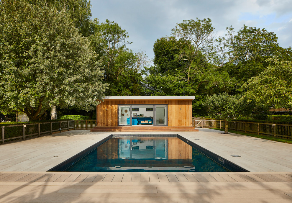 Modelo de casa de la piscina y piscina actual rectangular en patio trasero con entablado