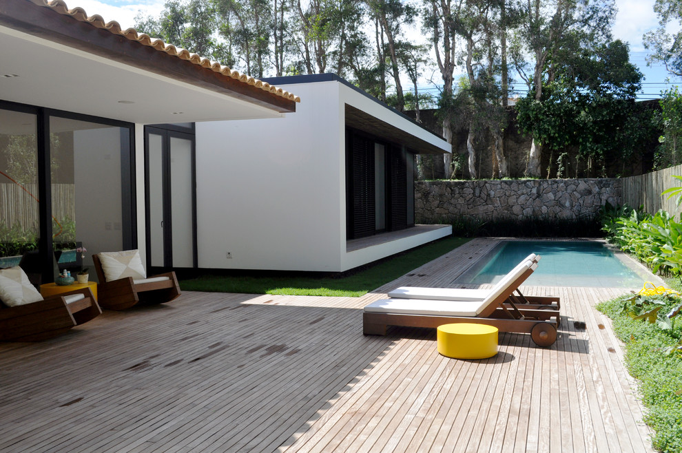 На фото: бассейн на заднем дворе в современном стиле с настилом и забором с