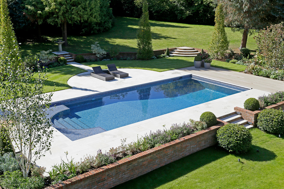 На фото: большой прямоугольный бассейн на заднем дворе в классическом стиле с покрытием из плитки с