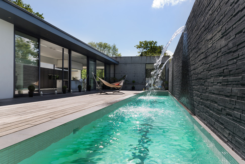 Inspiration for a modern rectangular lengths swimming pool in London with a water feature and decking.