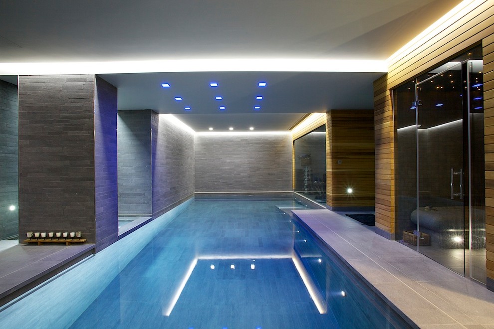 Medium sized modern indoor l-shaped lengths swimming pool in London with natural stone paving.