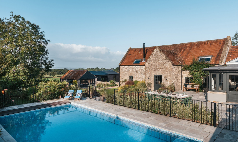 Large rural back rectangular swimming pool in Other with natural stone paving.