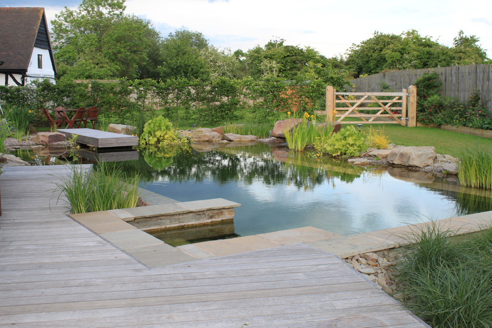 Photo of a large farmhouse back rectangular natural swimming pool in Other with a water feature and natural stone paving.
