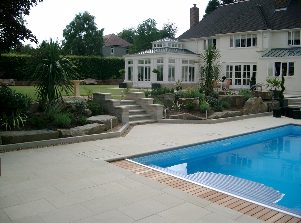 Foto på en stor pool på baksidan av huset, med naturstensplattor