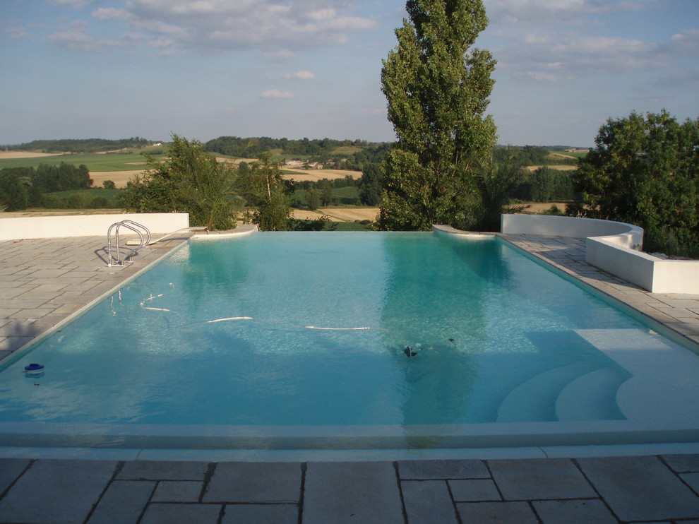Cette image montre une piscine sur toit à débordement méditerranéenne de taille moyenne et rectangle avec un point d'eau et des pavés en pierre naturelle.