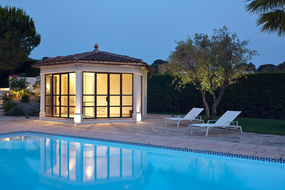 На фото: большой прямоугольный бассейн в средиземноморском стиле с домиком у бассейна и покрытием из каменной брусчатки с
