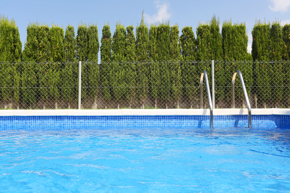 Ejemplo de piscina con fuente mediterránea pequeña en forma de L en patio trasero con losas de hormigón