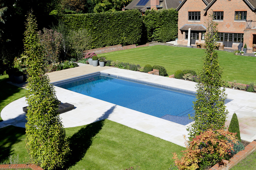 Modelo de piscina clásica grande rectangular en patio trasero con suelo de baldosas
