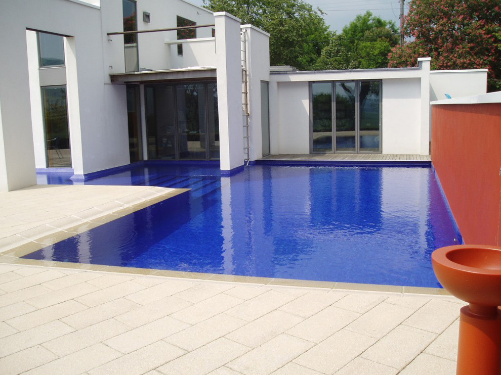 Ejemplo de piscina natural de estilo de casa de campo de tamaño medio en forma de L en patio trasero con adoquines de hormigón