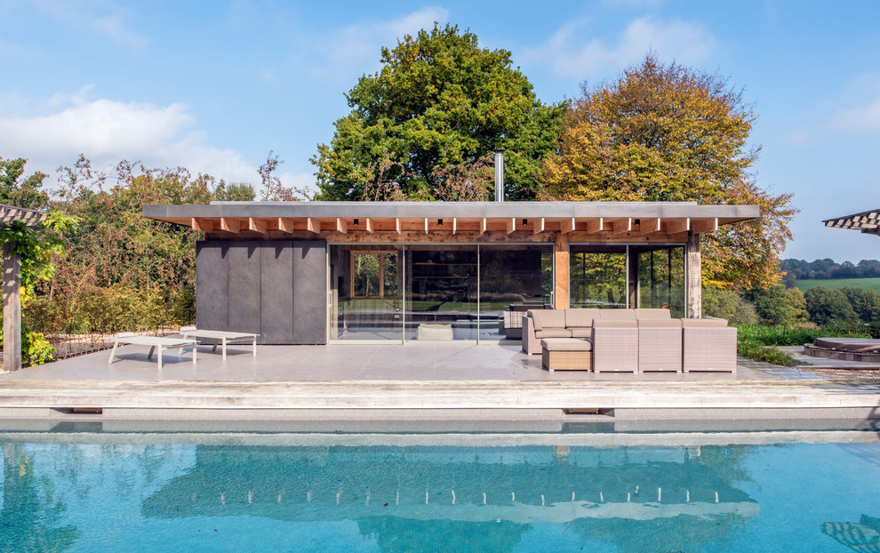 Photo of a large contemporary back rectangular lengths swimming pool in Sussex with a pool house and natural stone paving.
