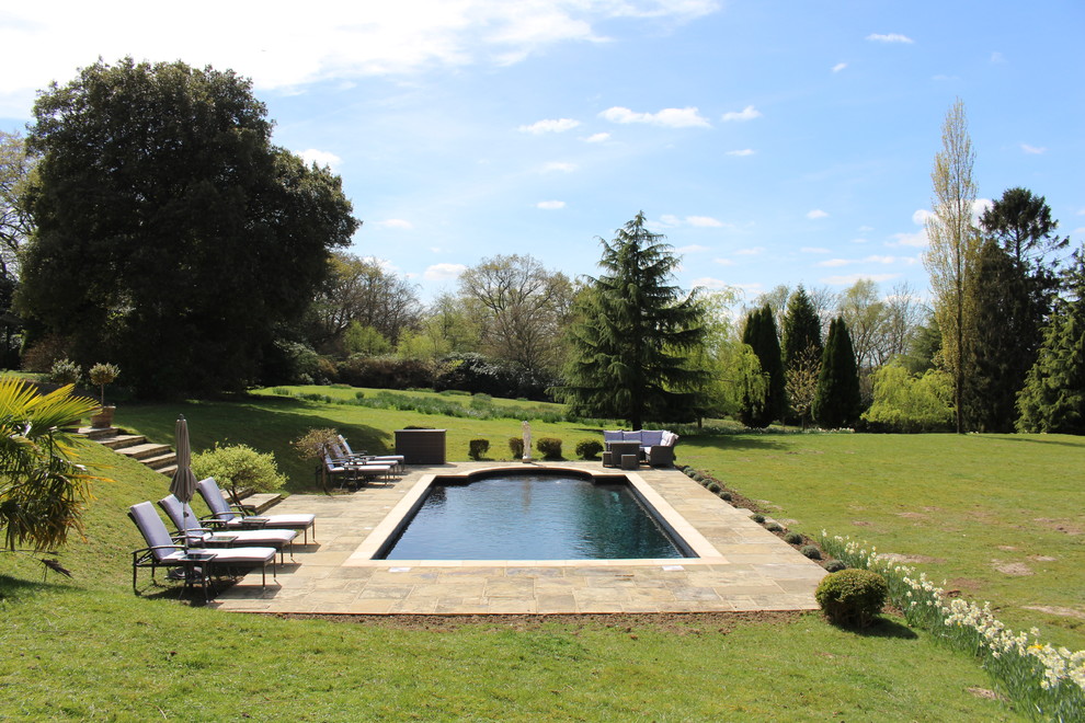 Ejemplo de piscina alargada tradicional a medida en patio trasero con suelo de baldosas
